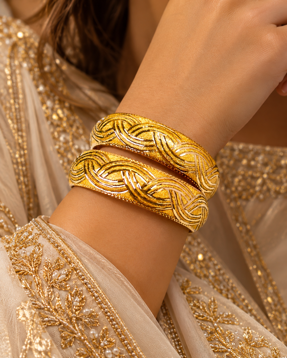 Pair of wide gold bangles with a braided, diamond-cut pattern worn on the wrist