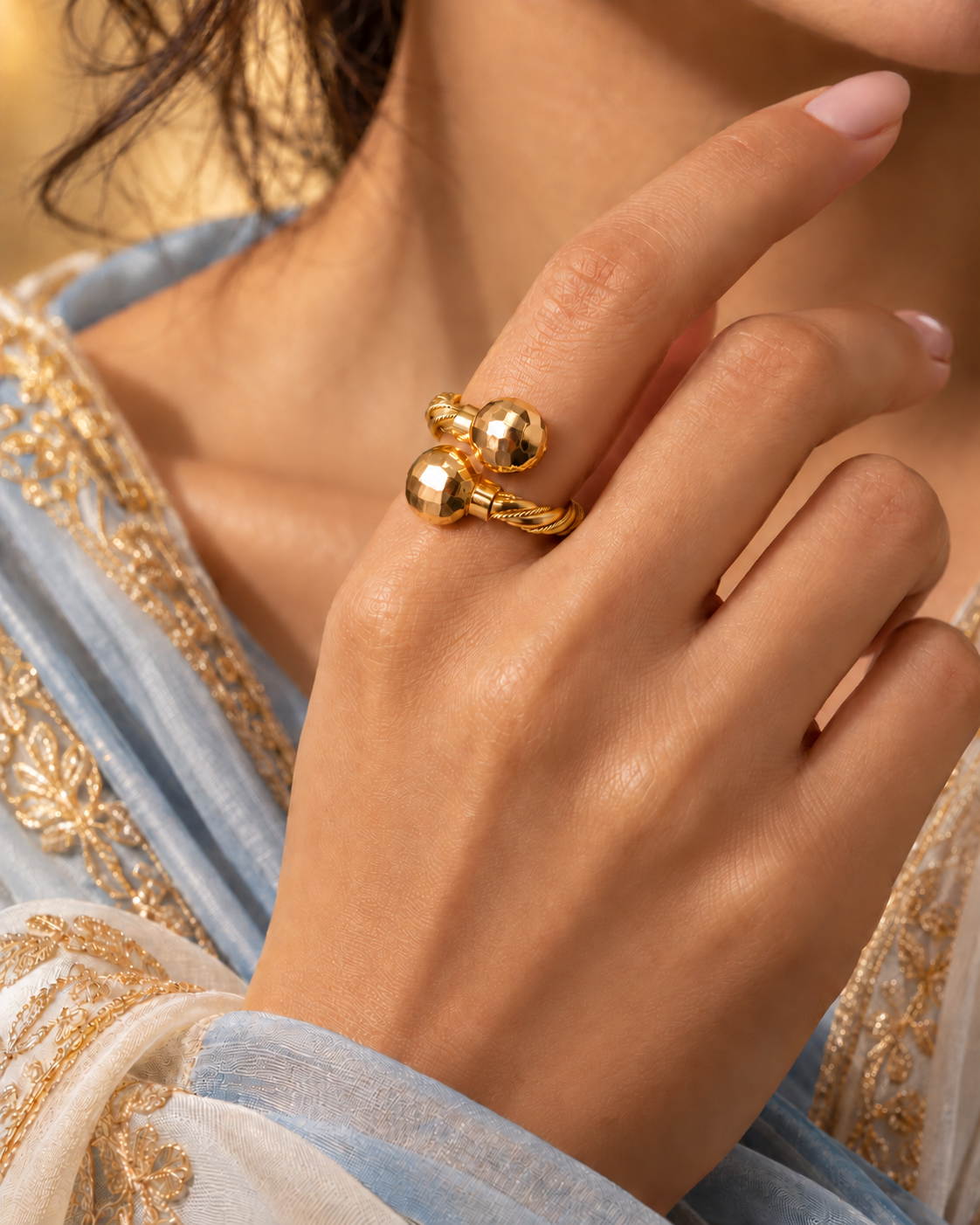 Gold twisted rope bypass ring with two diamond-cut gold beads, worn on the hand